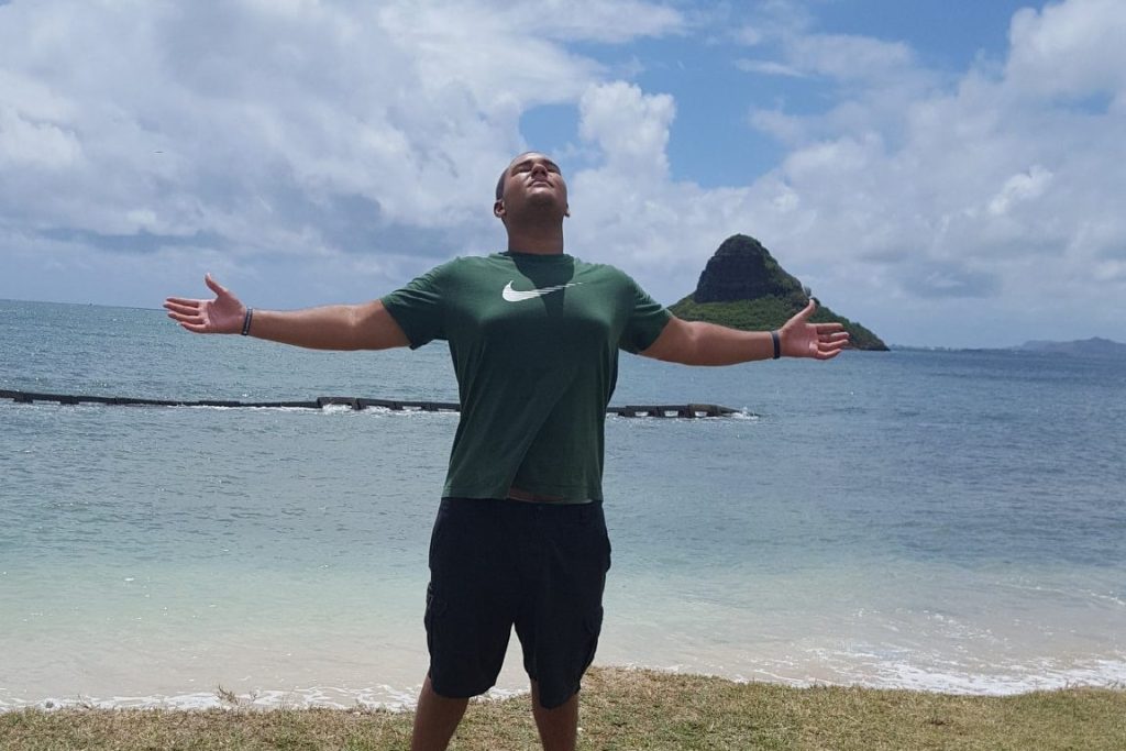 teen boy standing on beach in Hawaii with arms outstretched