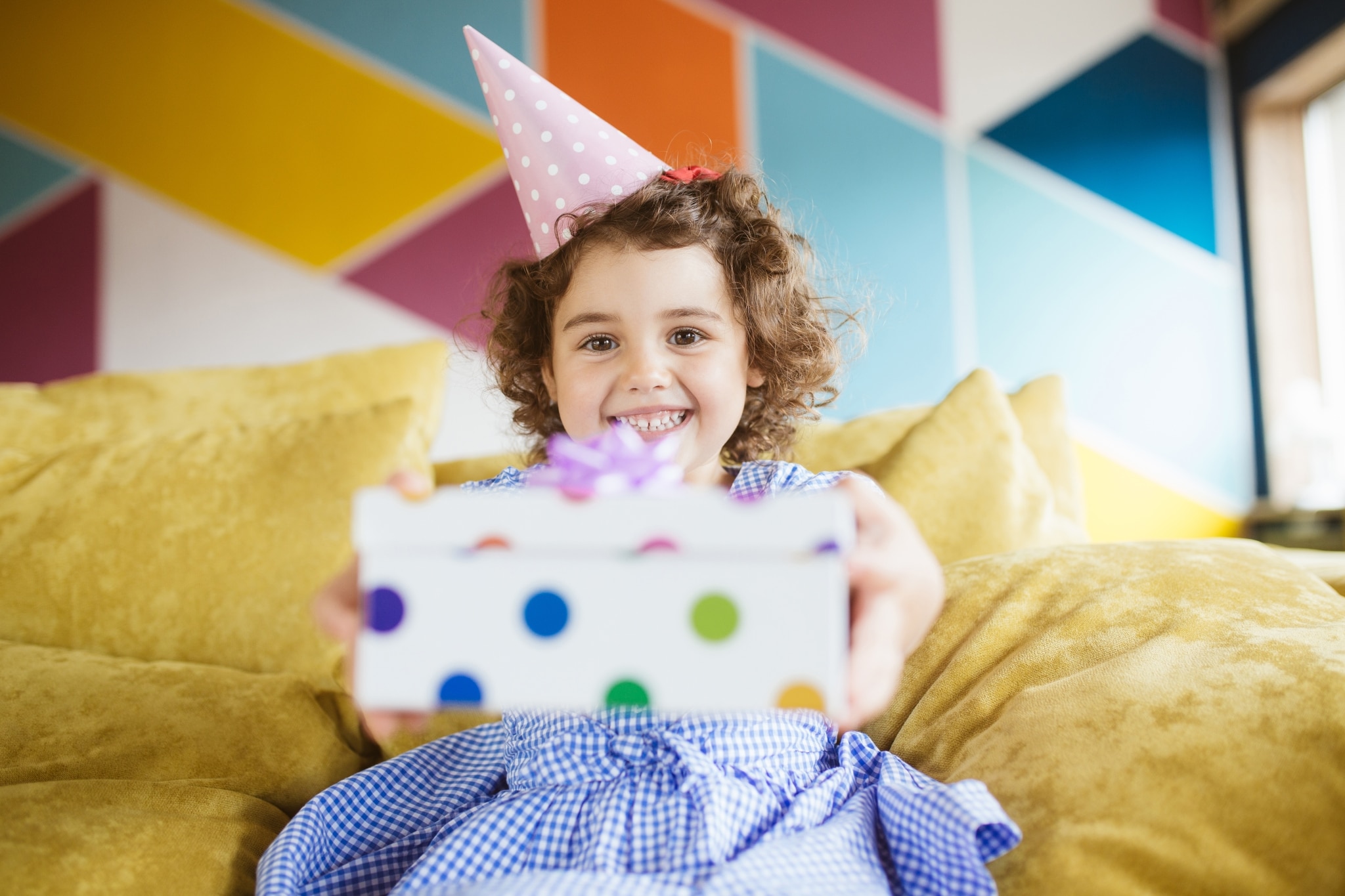 little girl wearing party hat and holding birthday present