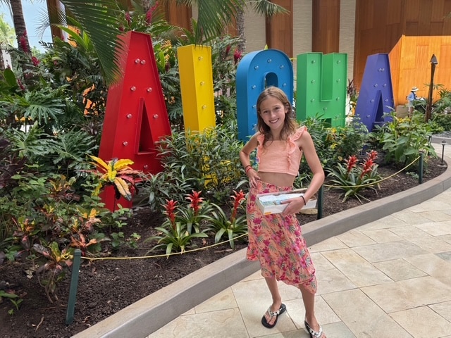Wish Kid Caiya next to "Aloha" sign on her Hawaii wish trip